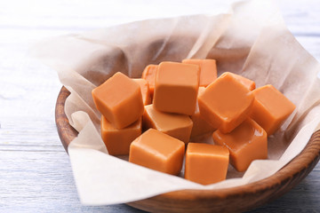 Bowl with tasty caramel candies on wooden background