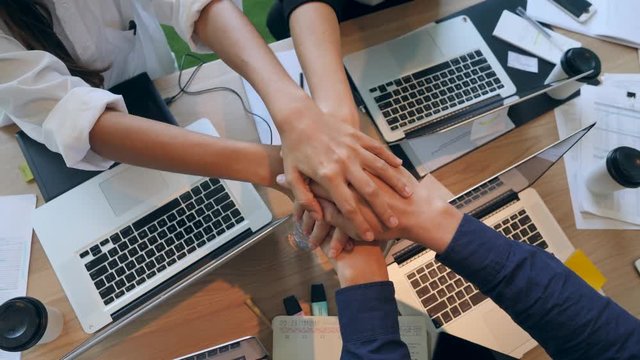 Group of Young Mixed Race People Making Hands in Stack in Office. Wooden Table Desktop View from Above. 4K.