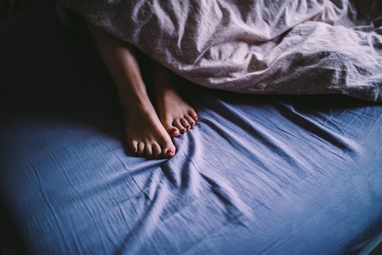 Close-up of feet sticking out of blanket in bed