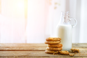 Chocolate chip cookies, bottle and glass of milk on wooden table near window, white background. Sunny morning, copy space