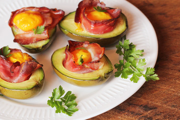 Avocado Egg Boats with bacon on white plate. Wooden background. Top view