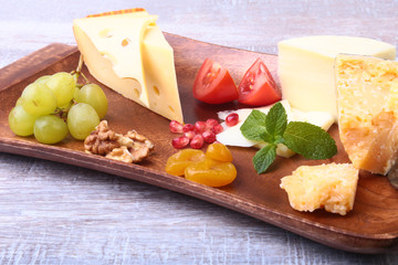 Assortment of cheese with fruits, grapes, nuts and cheese knife on a wooden serving tray.