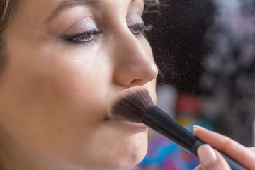 Process of applying makeup on the girl's face close-up. Application of powder with a special brush