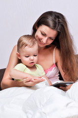 a young mother with a small child sitting on a bed under a white blanket and look at the hands each other
