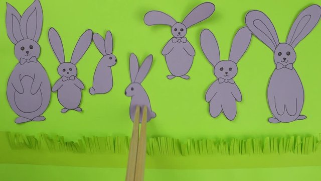 Figures of rabbits from paper of violet color move on a green background