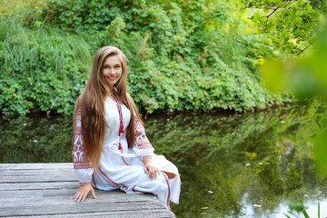 Beautiful slavonic girl with long blond hair and blue eyes sitting near river