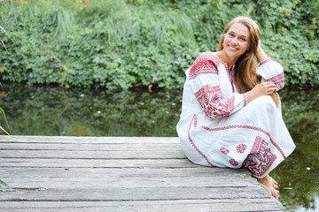 Naklejka premium Beautiful slavonic girl with long blond hair and blue eyes sitting near river