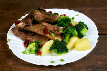 roasted pork ribs with potatoes and broccoli on an old wooden table