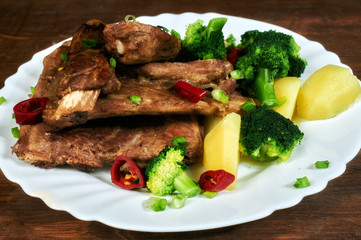 roasted pork ribs with potatoes and broccoli on an old wooden table