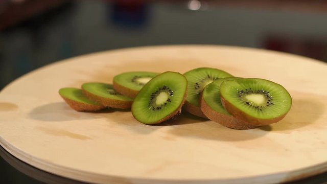 Close-up of slices of kiwi on chopping board. Close-up of sliced kiwi lying on wooden cutting Board on a black background. A slow camera movement from left to right.