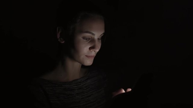 Closeup view of a woman using her phone in a dark room, chatting in the darkness with smartphone, communicating with friends online