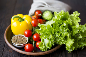 fresh organic vegetables: tomatoes, peppers, cucumber, chili, spices and salad in a clay plate on the table dark wood