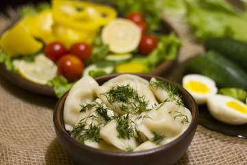 Closeup view of traditional russian food - pelmeni, ravioli or meat dumplings. Served with eggs, tomatoes, salad, marinated mushrooms, sauerkraut, cucumbers, green onion and garlic. Copy space