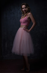 Dark light. A young amazing girl in a beautiful vintage pink outfit with a chic hairstyle, smiling, posing and looking at the camera.
