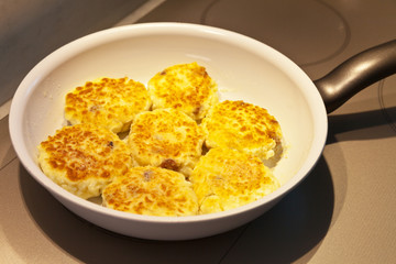 Curd cheese cakes with  raisins are fried in a frying pan on an induction cooker