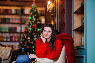 Beautiful girl in a red sweater near the Christmas tree.