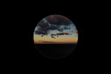 view through round porthole scuttle on dawn at sea