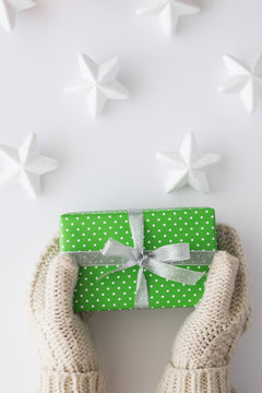 Woman hands in mittens holding green gift box with white stars isolated on white background. Top view, flat lay. Copyspace.