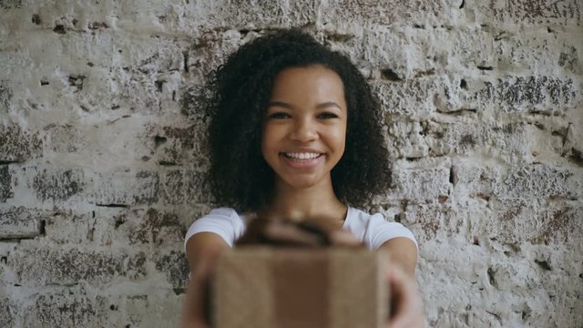 Portrait of curly african american girl present gift box and smiling into camera