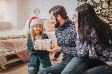 Merry Christmas and Happy Holidays! Cheerful Mother, father and her cute daughter girl exchanging gifts. 