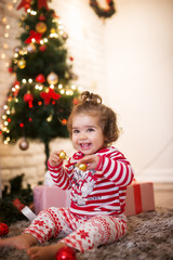 Curly small child girl with ponytail playing with ornaments while sitting on a carpet for Christmas holidays.