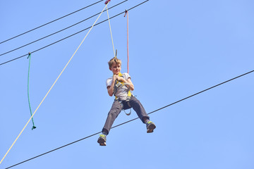 Cute school boy enjoying a sunny day in a climbing adventure activity park. Clear blue sky background. Children summer activities.