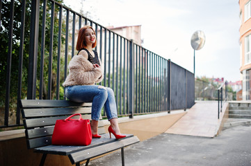 Red haired girl with red handbag posed on bench.