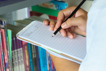 Close up hands of librarian holding notebook with black pencil in library. Used to record book information and number of books. Education concept. Blur background.
