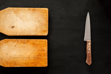 Two empty wooden cutting boards with knife on a dark background, top view