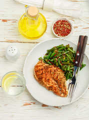 Grilled chicken breast (fillet) and green beans with spices in a white plate on a wooden table. Selective focus. Top view