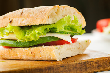 Vegetarian sandwich with avocado, tomato, egg and green salad on a wooden board