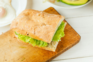 Vegetarian sandwich with avocado, tomato, egg and green salad on a wooden board