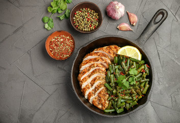 Grilled chicken breast (fillet) and green beans with spices in a cast iron skillet on the black stone table. Selective focus. Copy space