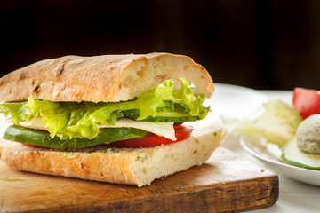 Vegetarian sandwich with avocado, tomato, egg and green salad on a wooden board