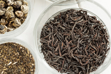 Fototapeta premium Different dry tea in a small glass dishes on a white wooden table, top view