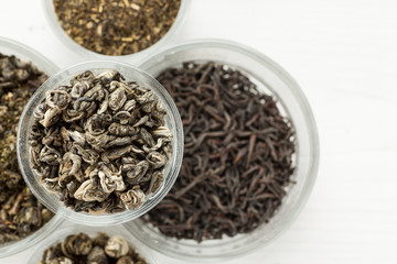 Different dry tea in a small glass dishes on a white wooden table