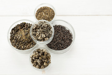Different dry tea in a small glass dishes on a white wooden table
