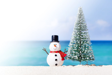 Snowman toy and fir tree at white sandy beach