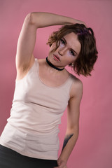 Portrait of young woman in shirt and choker holding arm over her head. Pink background