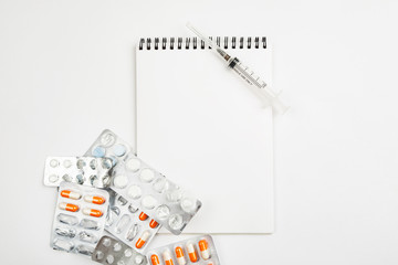 Blank notepad among different medications on a white background, template for text