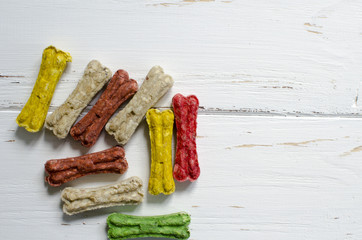 Delicious chewing colored bones for dogs with different tastes on white wooden background