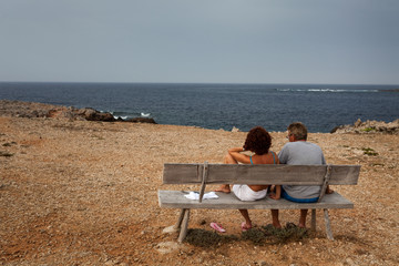 Pareja sentada en un banco mirando al mar