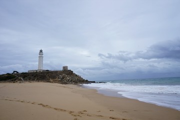 Lighthouse on beach with waves and clouds