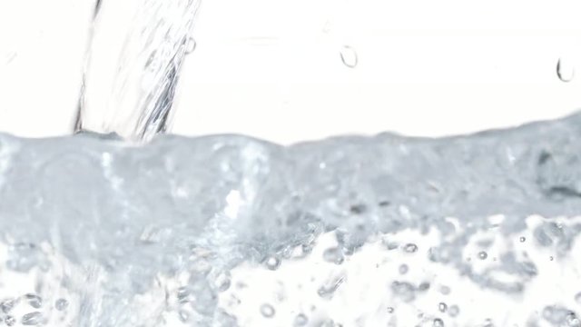 Macro footage of water pouring in a transparent container. White background. Close-up macro shot.