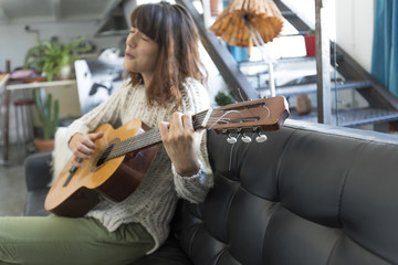 Obraz na płótnie Canvas Beautiful woman sitting on a sofa and playing guitar