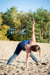 Woman practicing yoga in the sand - Extended Side Angle Pose &mdash; Utthita Parsvakonasana - Autumn day