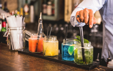 Bartender hand at multicolored fashion drink with straw on vintage glass cups in fashion cocktail bar - Food and beverage concept with professional barman working at mixology restaurant - Vivid colors © Mirko Vitali