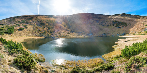 Panorama of mountains lake with reflection in blue water, morning light and shining sun