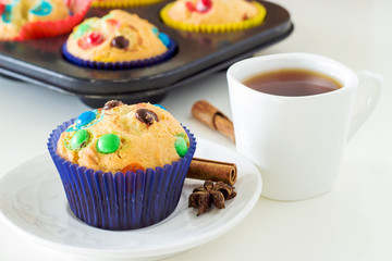 Homemade Muffins with colorful chocolate chips and a cup of black tea. White background. Front view. Selective focus.