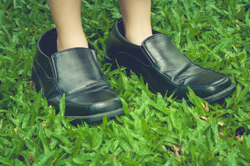 Legs of cute girl wearing black business shoes and standing on green grass in vintage style.